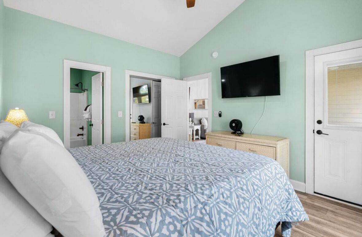 Une chambre à coucher avec un lit, un téléviseur fixé au mur et une porte donnant sur une salle de bain.