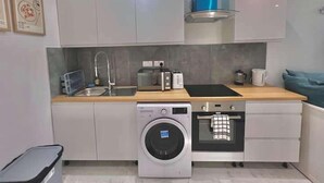 A compact kitchen with white cabinets, a washing machine, an oven, and a microwave. - Kings Cross 1 Bedroom Apartment (London)