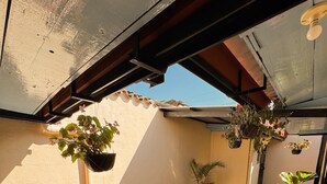 A rooftop patio with a concrete floor, a wooden bench, and hanging planters with various plants. - Casita Sol (Antigua Guatemala)