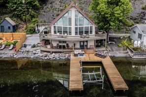 A large, modern house with a prominent glass facade, a wooden deck, and a dock extending into a calm body of water. - Sail Away Home: Serenity Awaits with Sprawling Sunset Views (Aurora)