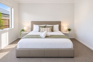 A bedroom with a large bed, two bedside tables with lamps, a window with a view of a fence, and a plant on each table. - Serene 4-bedroom house with AC in charming Park Ridge (Park Ridge)