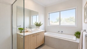 Un baño moderno con cabina de ducha de vidrio, lavabo con espejo, bañera y ventana que proporciona luz natural.