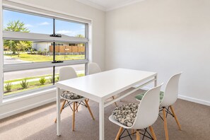 Una habitación con una mesa y sillas blancas, ventanas amplias y piso alfombrado.