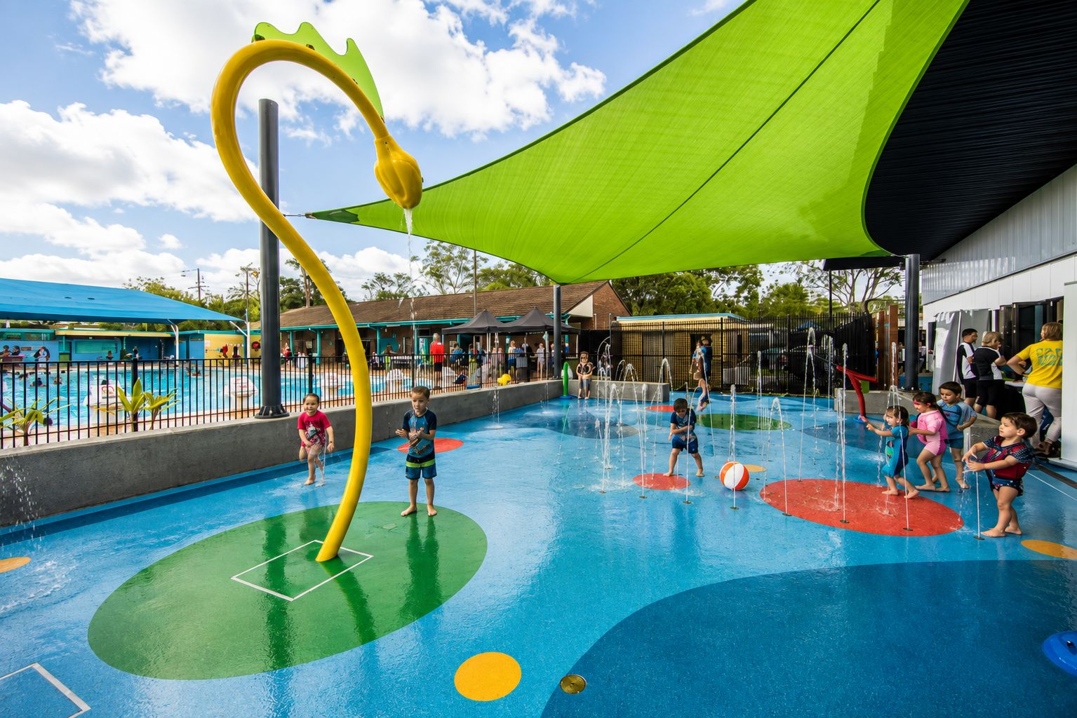 Un espace de jeux aquatiques en plein air comprenant une piscine, des toboggans et une grande zone ombragée par une végétation luxuriante.