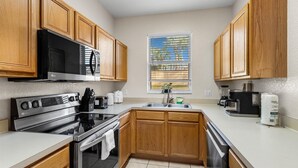 A modern kitchen with wooden cabinets, stainless steel appliances, and a window with blinds. - Disney escape 4BR Townhome + Resort (Davenport)