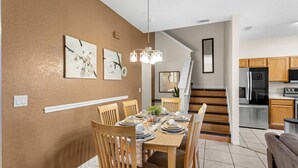 A dining area with a wooden table set for four, flanked by two chairs. A staircase leads to a kitchen area with modern appliances. - Disney escape 4BR Townhome + Resort (Davenport)