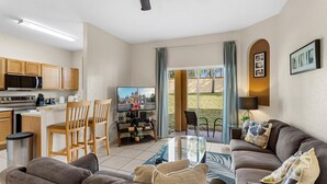 A compact living space with a kitchenette, a dining area, a seating area with a sofa and chairs, and a large window offering a view of the outdoors. - Disney escape 4BR Townhome + Resort (Davenport)