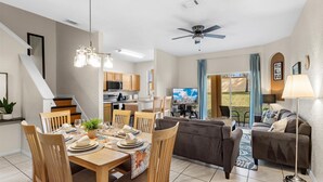 A modern living room with a dining area, a kitchen, and a balcony with a view. - Disney escape 4BR Townhome + Resort (Davenport)