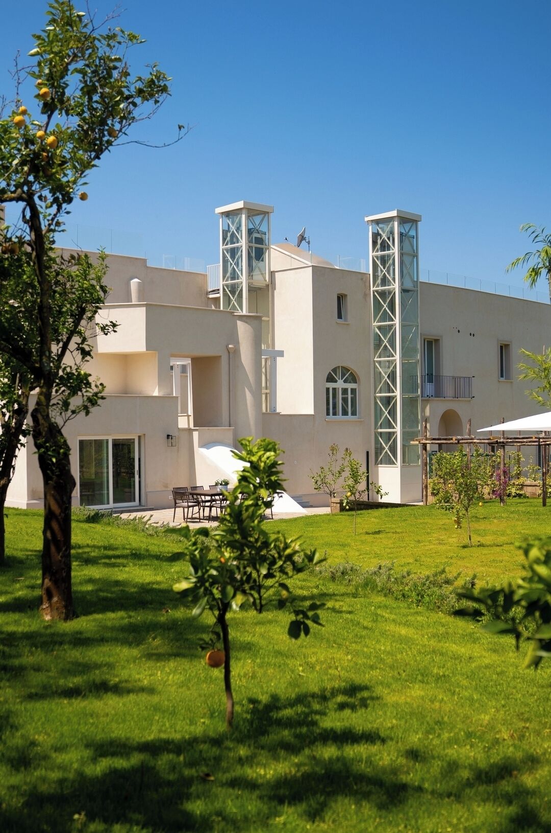 A modern building with a flat roof, two tall towers, and a well-maintained lawn with trees.