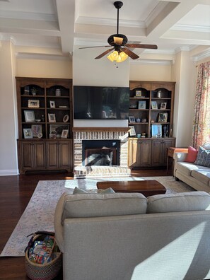 A living room with a fireplace, a ceiling fan, and a large flat-screen TV. - Perfect Masters Rental - 5-bedroom/3.5 bath home in Evans. Easy commute to ANGC (Evans)