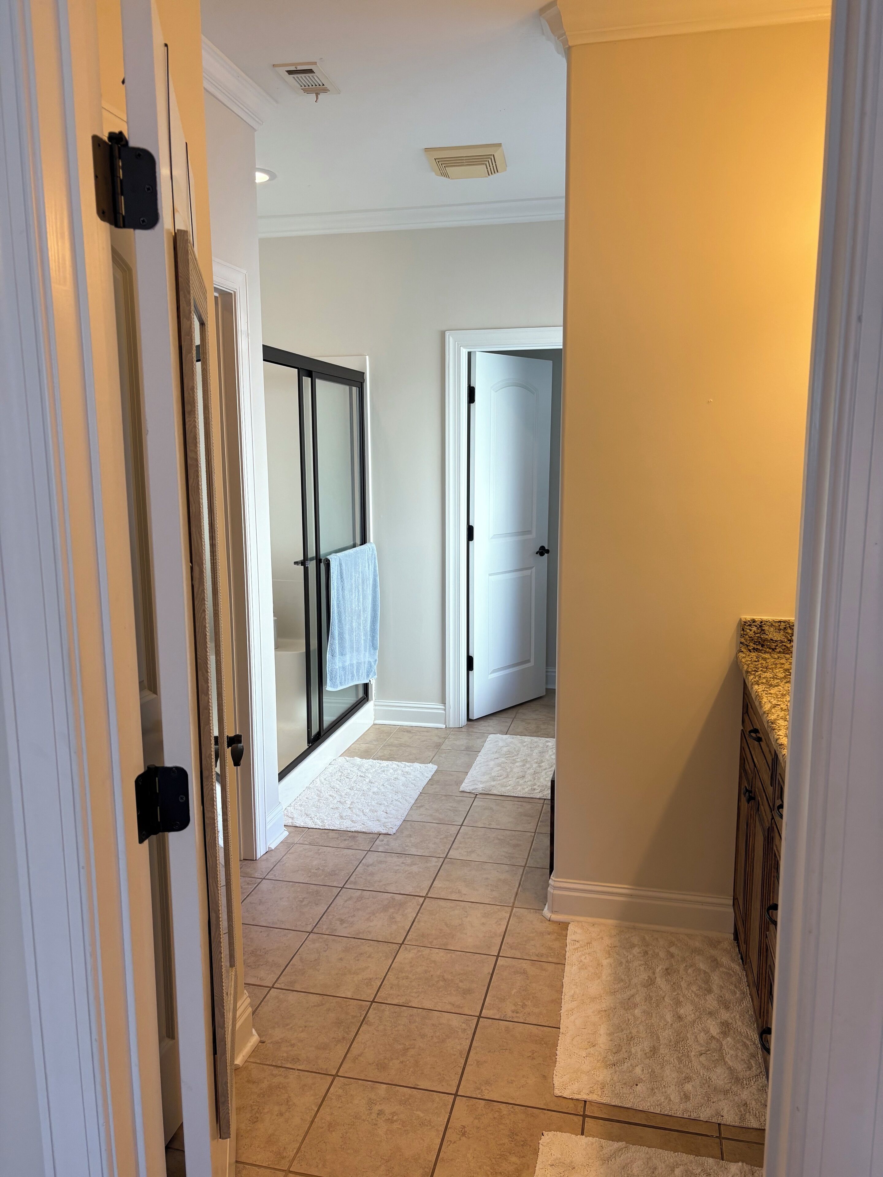 Un couloir avec une porte en verre donnant sur une salle de bain, une porte blanche et un sol carrelé.