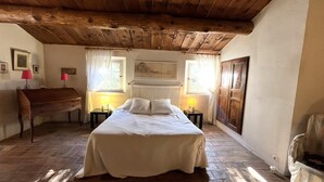 Quarto com cama, escrivaninha de madeira, duas luminárias de cabeceira e uma janela grande com cortinas.