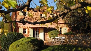 Uma casa rústica com fachada de pedra, um pequeno alpendre e um jardim bem cuidado.