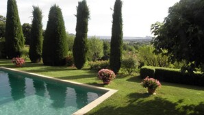 Uma piscina cercada por grama bem cuidada e árvores altas e esguias.