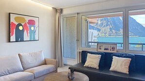 Ein modernes Wohnzimmer mit einer Couch, einem Couchtisch und einem großen Fenster mit Blick auf eine gebirgige Küstenlandschaft.