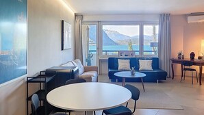 Ein modernes Wohnzimmer mit einer Couch, einem runden Tisch und Blick auf einen See und Berge.