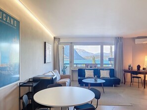 Ein modernes Wohnzimmer mit einer Couch, einem runden Tisch und Blick auf einen See und Berge.