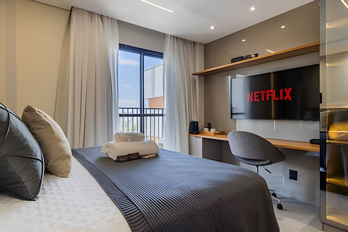 Quarto de hotel moderno com cama, escrivaninha, cadeira, TV e varanda.