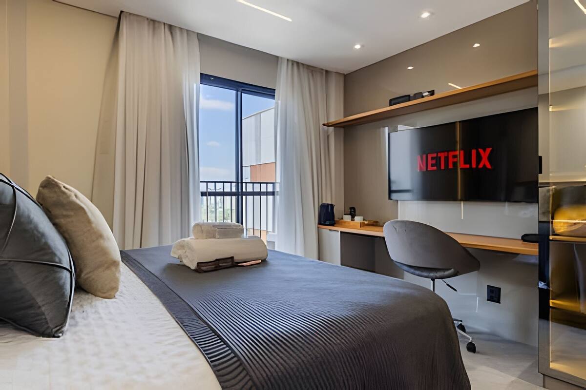 Una habitación de hotel moderna con cama, escritorio, silla, televisor y balcón.