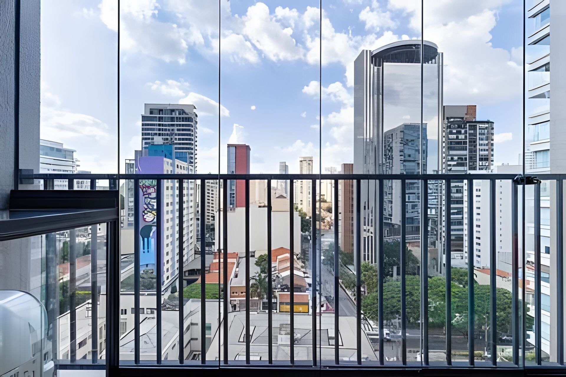Vista da cidade a partir de uma varanda, com edifícios modernos, céu claro e rua abaixo.