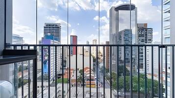 Vista da cidade a partir de uma varanda, com edifícios modernos, céu claro e rua abaixo.