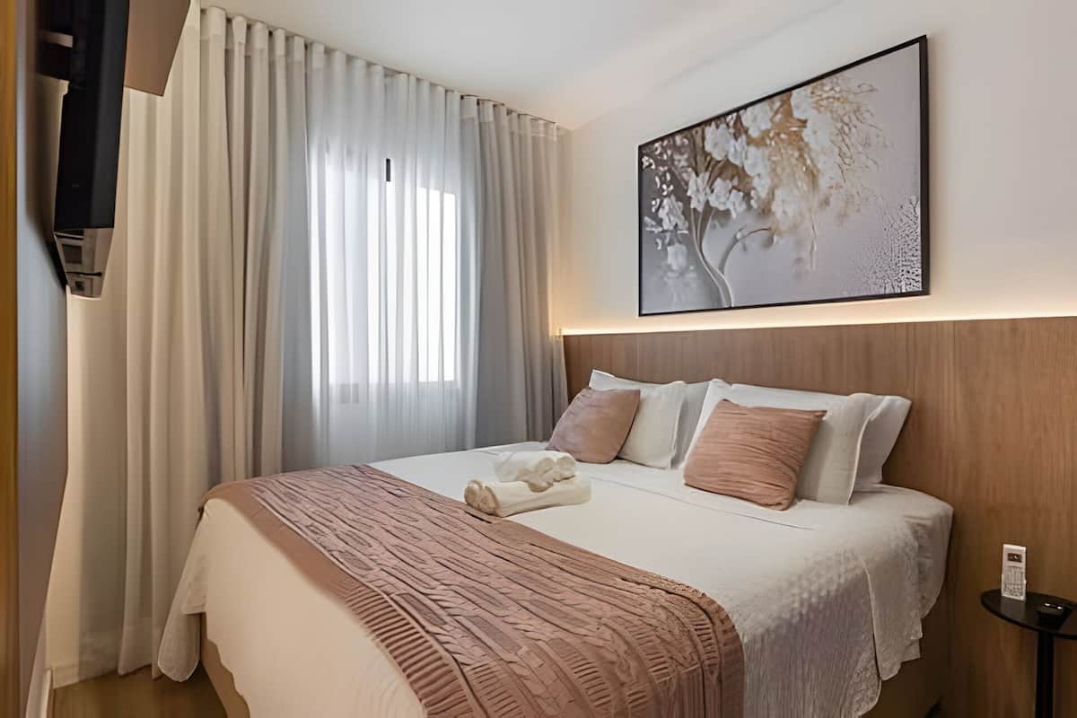 Una habitación de hotel con cama, cortinas, un cuadro y una mesita de noche.