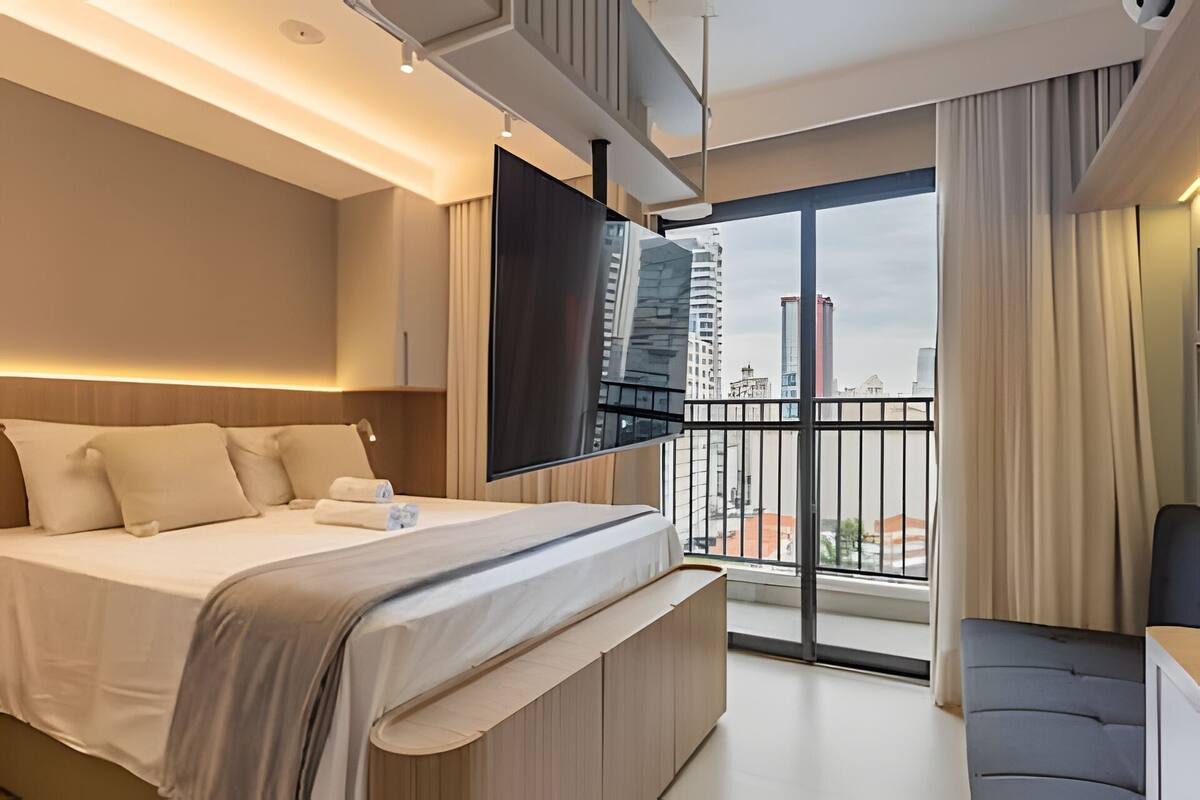 Una habitación de hotel moderna con una cama grande, un televisor de pantalla plana, un balcón con vistas a la ciudad y una zona de estar.