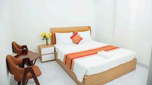 A hotel room with a wooden bed, white bedding, a small table with chairs, and a vase with yellow flowers. - Gia Bao Hotel Thu Duc (Ho Chi Minh City)