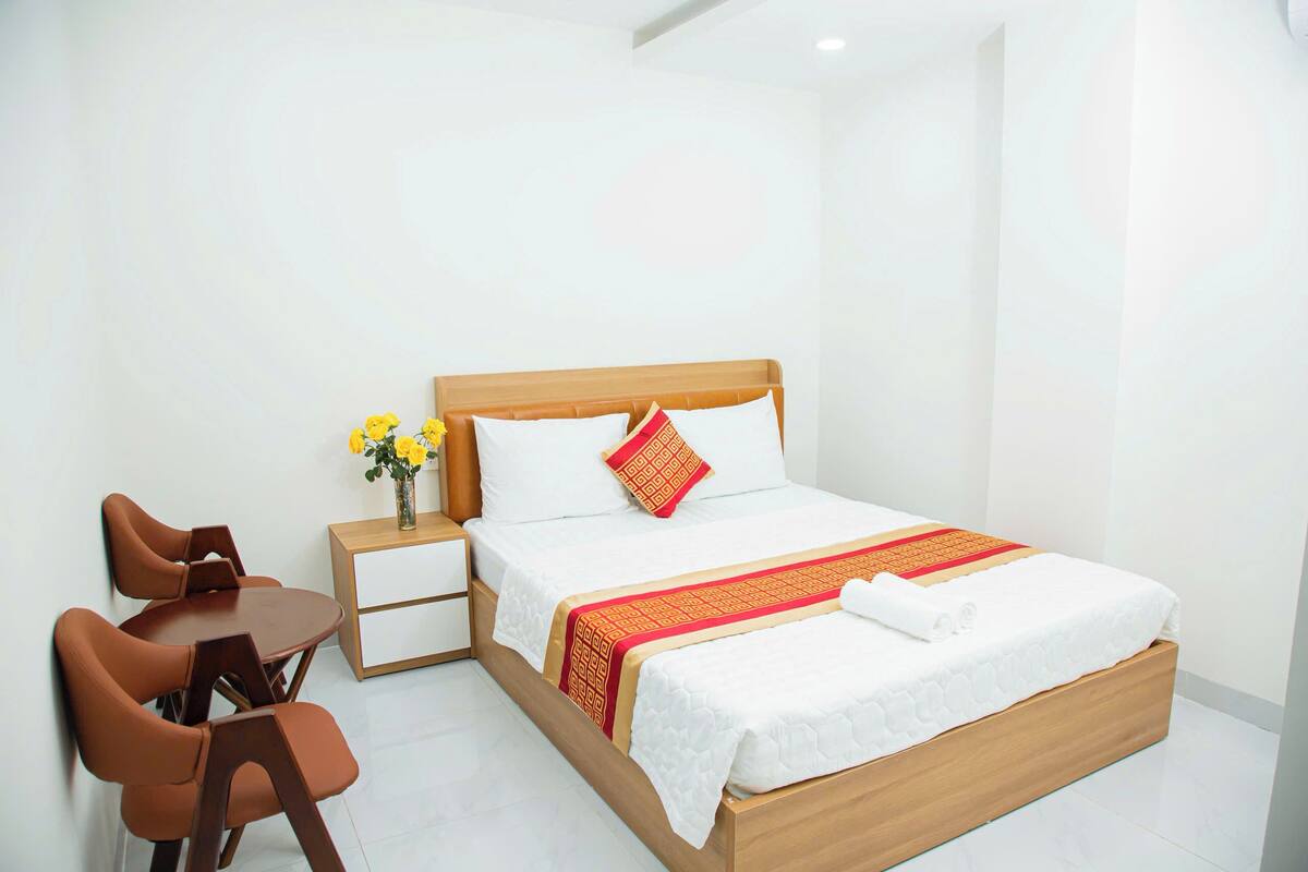 A hotel room with a wooden bed, white bedding, a small table with chairs, and a vase with yellow flowers.