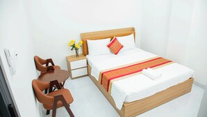 A hotel room with a wooden bed, white bedding, a red and yellow patterned blanket, a small bedside table with a vase of yellow flowers, and a wooden chair. - Gia Bao Hotel Thu Duc (Ho Chi Minh City)