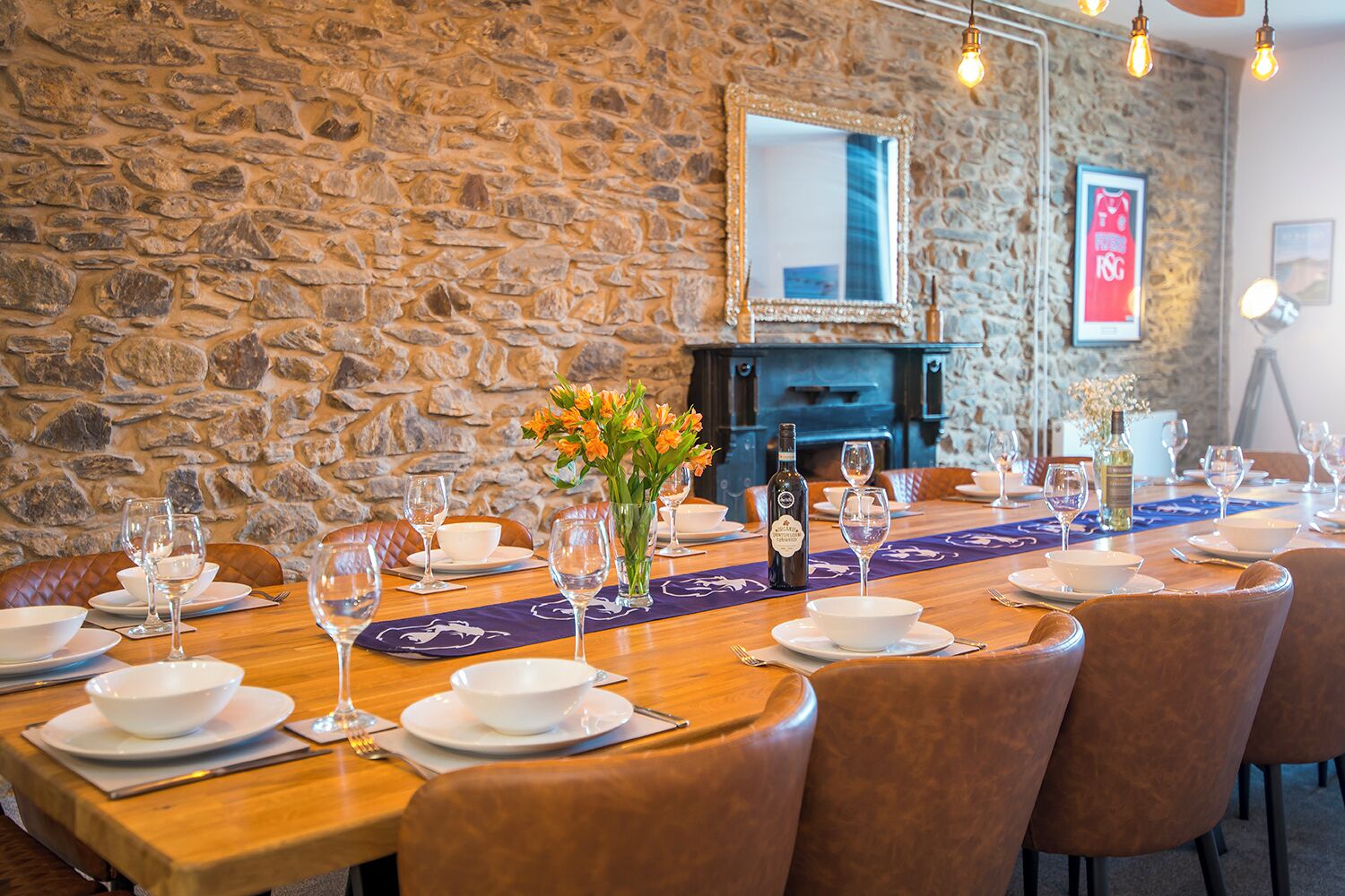 A dining area with stone walls, a fireplace, and a long table set for a meal.