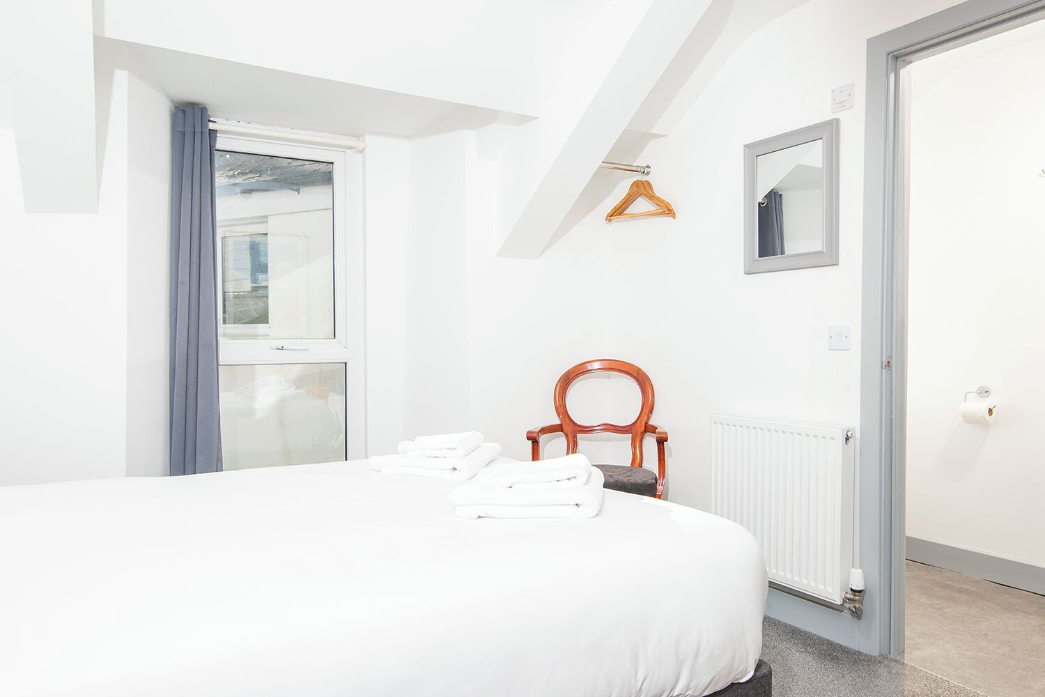 A bedroom with a bed, a chair, a radiator, and a window with curtains.