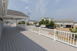 Um deck de madeira com guarda-corpo branco, com vista para um estacionamento com vários carros e um edifício de fachada branca.