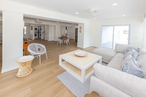 A modern living room with a sofa, a coffee table, and a dining area with chairs. - SEASIDE RETREAT - 8 bedroom semi-oceanfront with pool and ocean views (Virginia Beach)