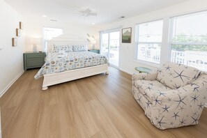 A bedroom with a bed, a nightstand, a chair, and a window with blinds. - SEASIDE RETREAT - 8 bedroom semi-oceanfront with pool and ocean views (Virginia Beach)