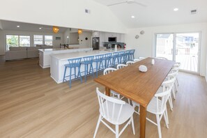 A spacious kitchen with a central island, white bar stools, and a dining table with white chairs. - SEASIDE RETREAT - 8 bedroom semi-oceanfront with pool and ocean views (Virginia Beach)
