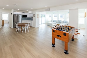 A spacious living area with a foosball table, a kitchen with modern appliances, and a seating area with a sofa and cushions. - SEASIDE RETREAT - 8 bedroom semi-oceanfront with pool and ocean views (Virginia Beach)