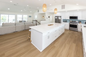 A modern kitchen with white cabinetry, stainless steel appliances, and a large island. - SEASIDE RETREAT - 8 bedroom semi-oceanfront with pool and ocean views (Virginia Beach)