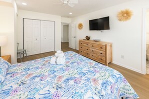 Quarto com uma cama, penteadeira, televisão e porta que dá para outro cômodo.