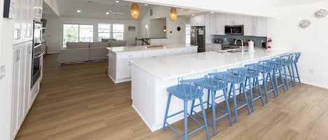 A modern kitchen with a large island, bar stools, and a view to the living area.