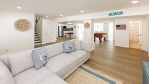 Ein modernes Wohnzimmer mit einer Eckcouch, Holzboden und einer Küche im Hintergrund.