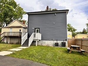 Une maison à deux étages avec un porche à l’avant, un escalier et un petit jardin devant.