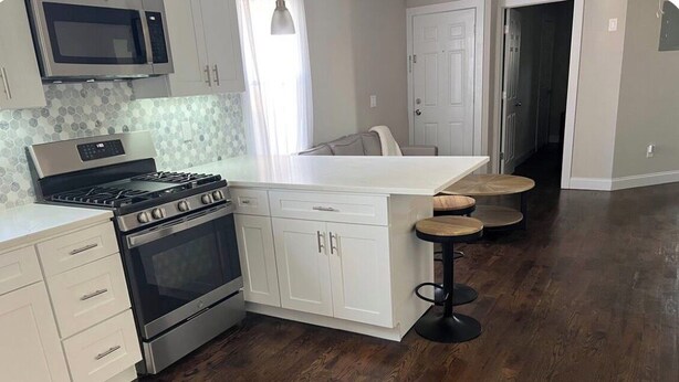 A kitchen with white cabinets, a stainless steel stove, and a wooden island with stools.