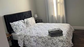 A neatly made bed with a floral bedspread, a dark headboard, and a folded towel on the bed.