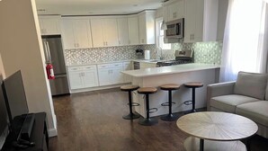 A modern kitchen with white cabinets, a central island with stools, a round dining table, and a bar area.