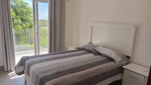Ein Schlafzimmer mit Bett, Nachttisch, Kommode und einer Schiebetür, die auf einen Balkon führt.
