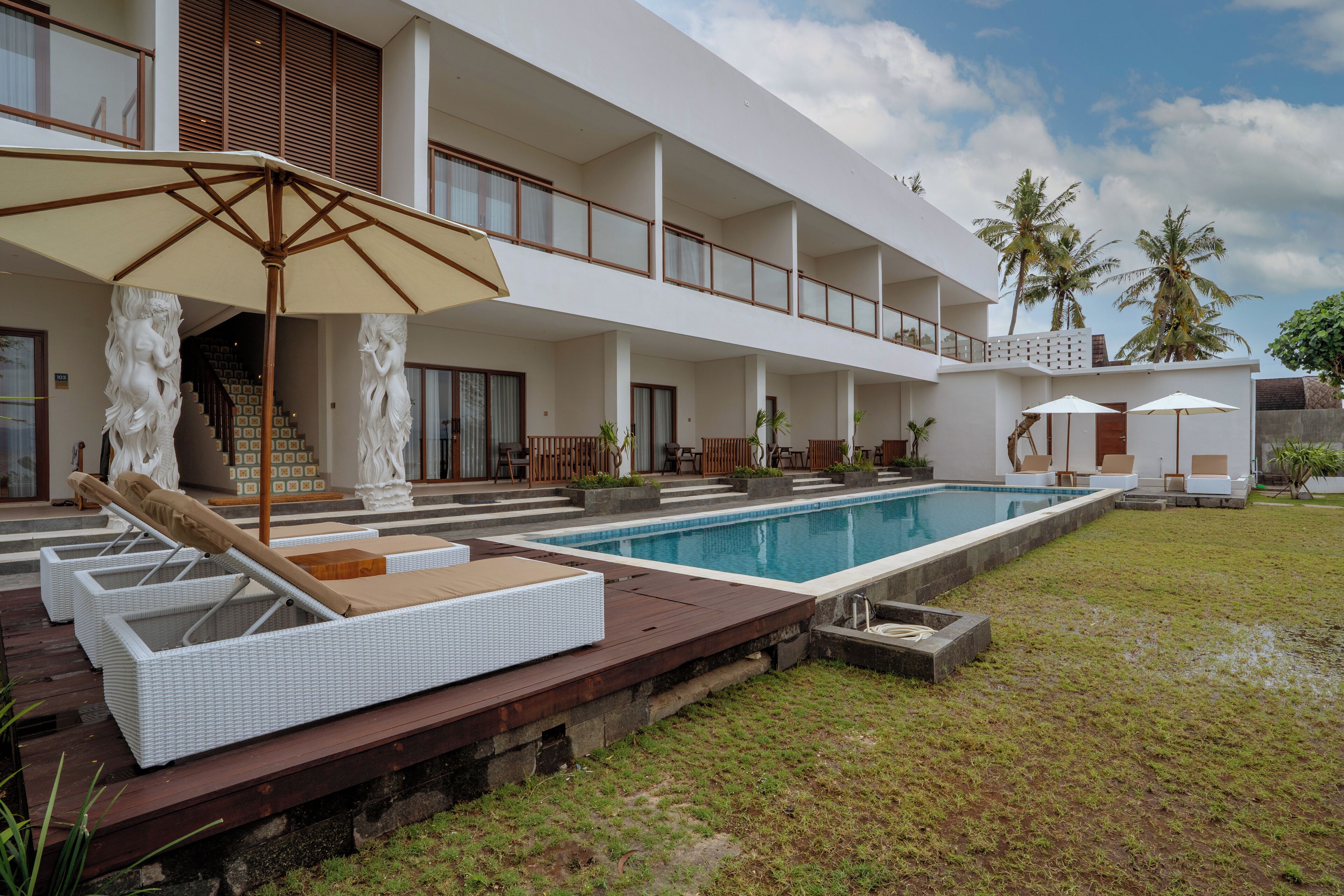 A modern hotel with a pool, outdoor seating, and a covered area with umbrellas.