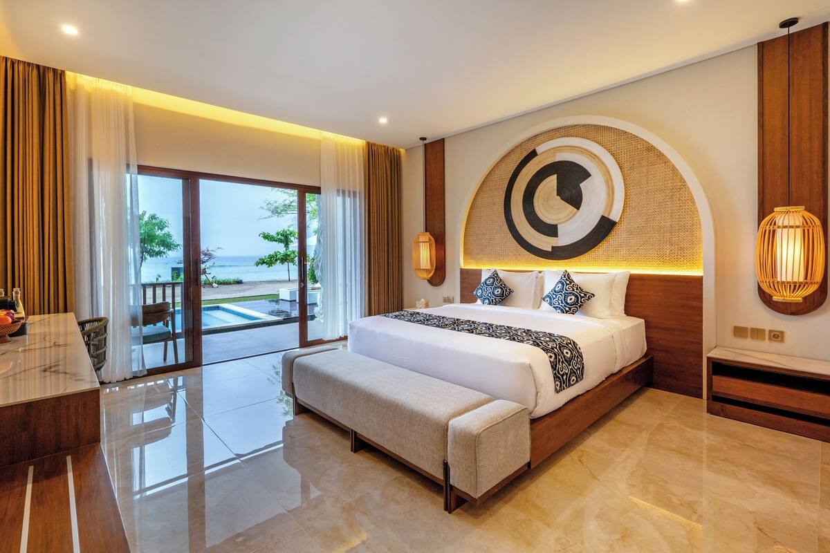 A modern hotel room with a large bed, a desk, and a view of the sea.