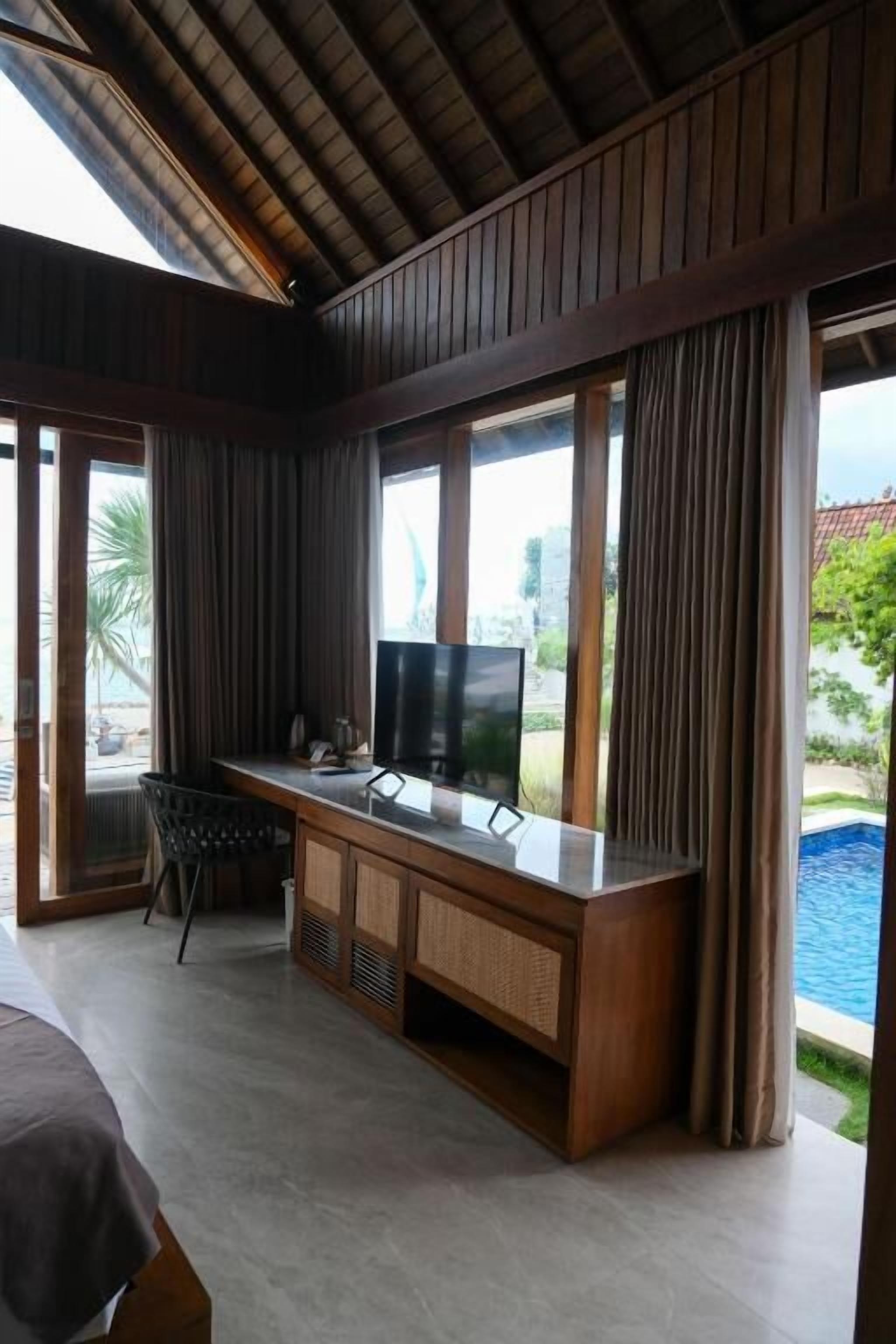 A room with a wooden desk, a television, and a view of a swimming pool.