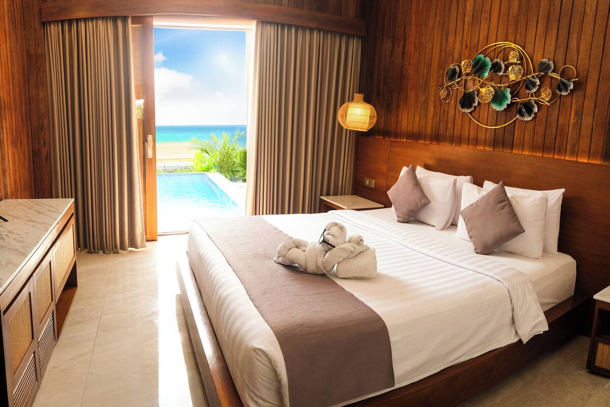 A hotel room with a large bed, a TV, a bedside table, and a view of the ocean.